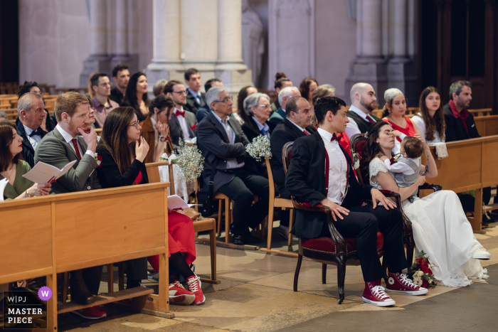 At a church in Lyon, during a ceremony, a baby playfully puts his fingers in the bride’s eyes, adding a humorous and candid touch to the wedding.