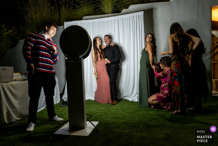At Tivoli Italian Villa in Fallbrook, CA, wedding guests gather at the photo booth during the reception, striking poses and enjoying the opportunity for lighthearted photos as part of the celebration.