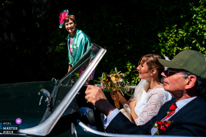 In the church parking lot of Brabant Wallon, Wallonie, the bride’s mother walks alongside the car driven by the father, capturing a candid and anticipatory moment before the wedding ceremony.
