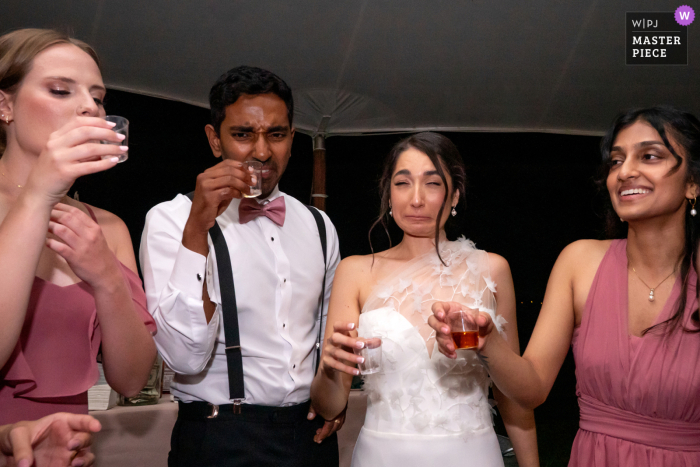 A candid moment captured at a private residence in Potomac, Maryland, as the bride cringes while she and her friends take a shot during the wedding reception, perfectly documenting the fun and lively atmosphere.