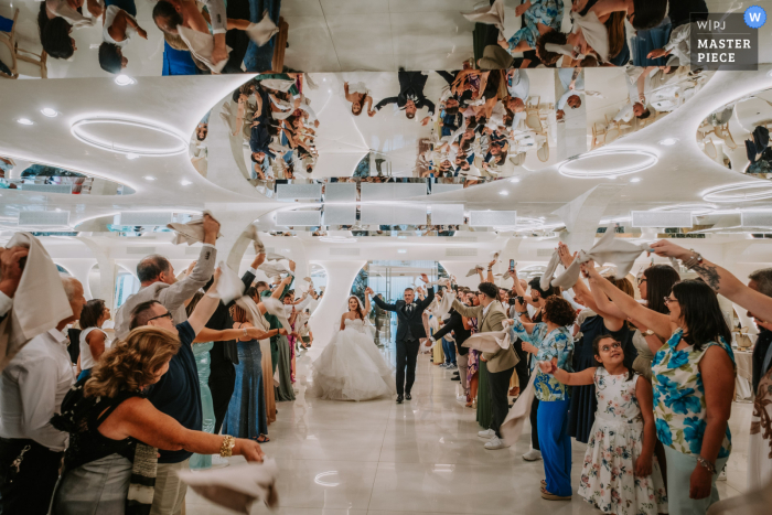   Cheers erupt at Giardino del Mago as guests wave napkins in the air, warmly welcoming the newlyweds upon their festive arrival at the mirrored reception venue.