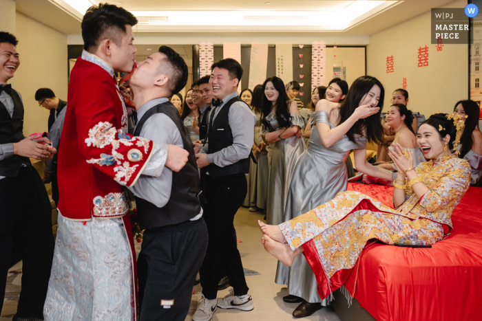 Groomsmen Are Roped Into Playful Bridal Games At A Hotel Suite, Drawing Competitive Laughter And Cheer From Bridesmaids. In a hotel suite, the groom and groomsmen approach the bride’s side, only to be roped into playful games by the bridesmaids, drawing laughter and spirited competition from everyone present.