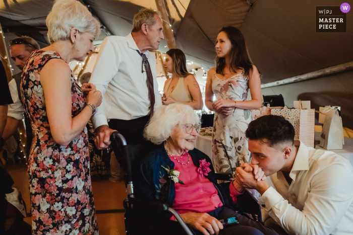   A tender gesture unfolds at the reception in Kent as the bride’s son leans in to kiss his grandmother’s hand, expressing love and connection across generations.