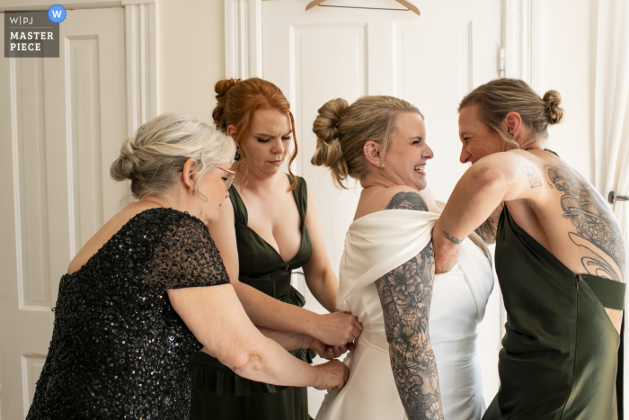   An intimate scene unfolds at an AirBnB in Savannah, Georgia, where the mother, sister, and a close friend carefully help the bride into her wedding dress before the ceremony.