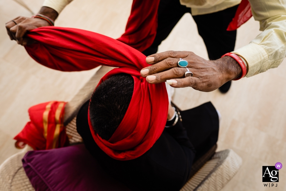 A high-angle detail shot of a hand tying a red wedding turban at the Waldorf Astoria Dubai