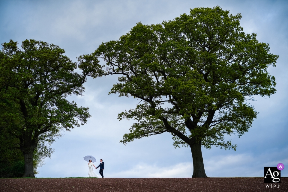 Foto von: <a href="https://www.wpja.com/photos/artistic-wedding-photographers/2548675"> Tom Beynon - Cambridge Cambridgeshire Schwalben nisten Scheune, Warwickshire-Hochzeitsfoto des Paares, während sie einen Spaziergang im Regen machen.