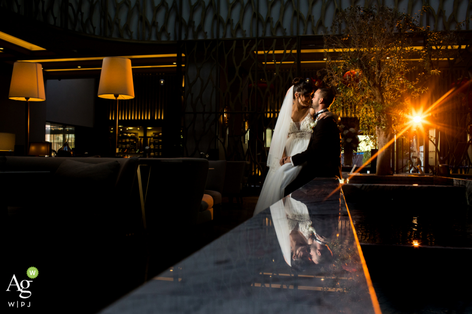 Fotografía del lugar de la boda de Hilton Ankara | Retrato del novio sentado justo al borde de una fuente en el vestíbulo de un hotel y la novia está a su lado.