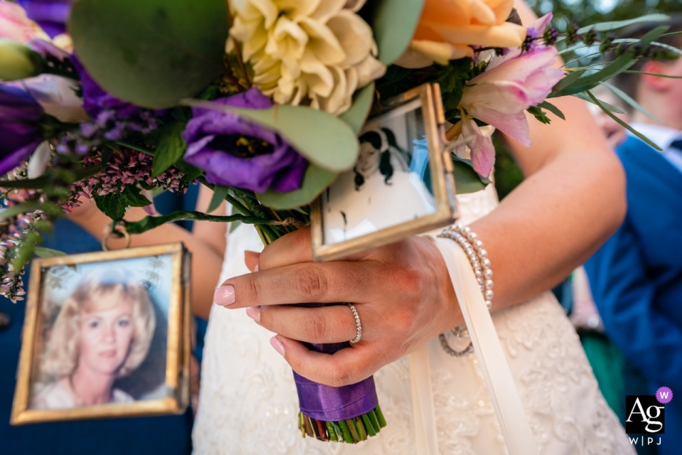 Foto von: <a href="https://www.wpja.com/photos/artistic-wedding-photographers/2559439"> Paul Tansley - Bordon Hampshire Farnham Castle, Surrey Hochzeit Detail Fotografie | Geschossen von den Bräuten schellen Sie, während Sie Blumenstrauß halten, Fotos von verstorbenen Verwandten in den Bilderrahmen auf Blumenstrauß. Nicht gestellt.