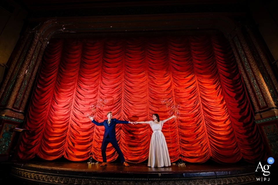 Foto von: <a href="https://www.wpja.com/photos/artistic-wedding-photographers/2559706"> Milan Lazic - Chicago Illinois Spieluhr Theater Hochzeit Bilder - Braut und Bräutigam Porträts auf der Bühne mit einem großen roten Vorhang.