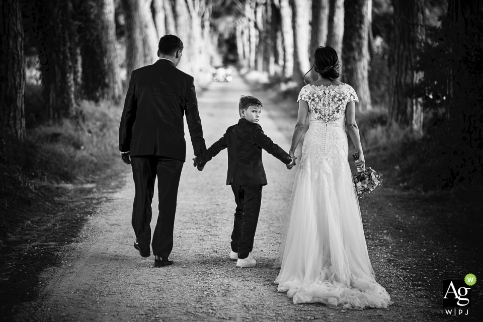 Foto de: Mirko Vegliò - Foligno Perugia Castello di Rosciano retrato de boda en blanco y negro de la novia, el novio y el niño caminando por el sendero arbolado