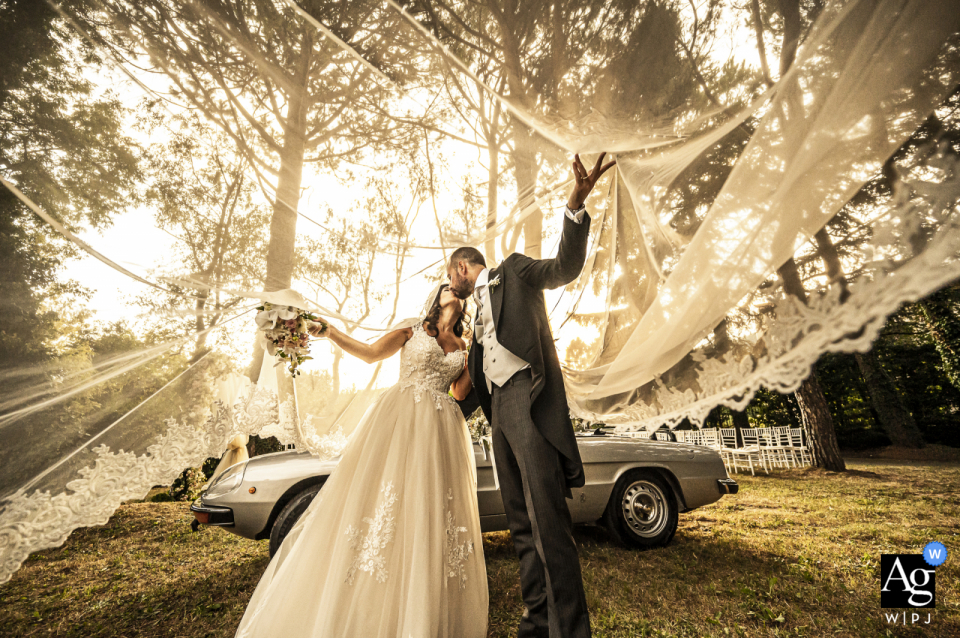 Regardez cette gracieuse image de Castello di Pomerio d'un doux baiser sous le voile près de la voiture ancienne, qui figurait parmi les meilleures photographies de mariage de la WPJA