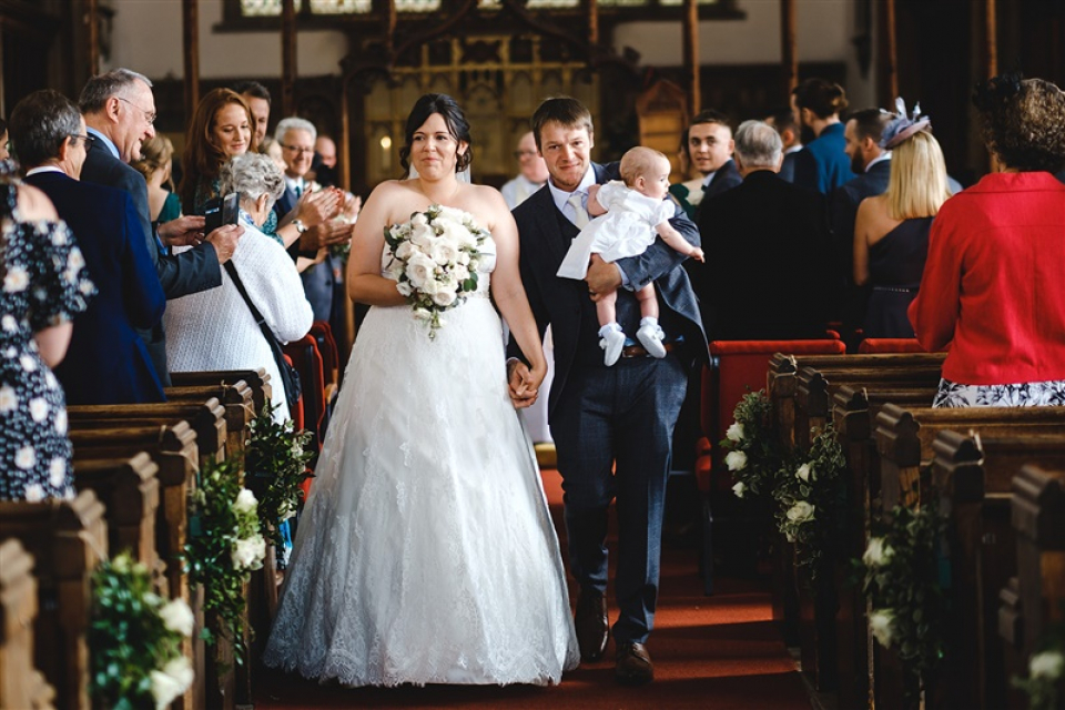 Un couple Beccles quittent leur cérémonie de mariage à l'église religieuse dans le Suffolk, UK Beccles, Suffolk, Royaume-Uni, les mariés sortent de leur cérémonie de mariage à l'église avec un bras de bébé