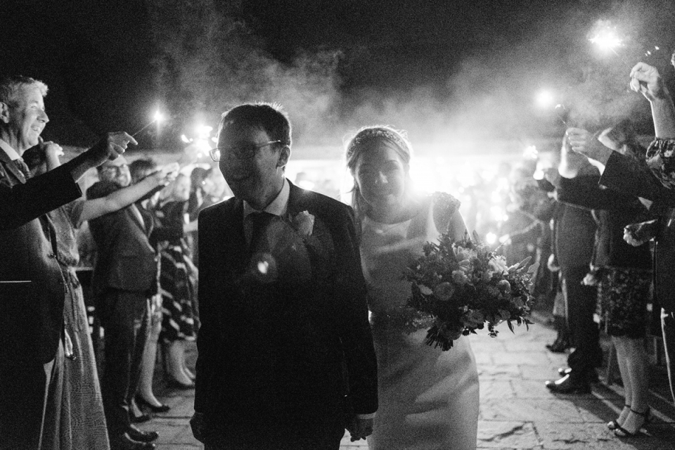 Le couple du Suffolk quitte sa réception de mariage nocturne sous des cierges magiques et à travers la fumée sur le site d'Easton Grange Easton Grange, Suffolk night wedding reception sparkler départ par les mariés