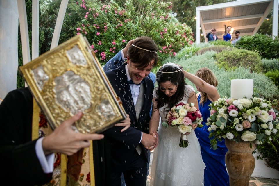 Der Zelebrant nimmt den Arm des Bräutigams und führt ihn und seine Braut um den Tisch Athen Hochzeit mit Zelebrant, Braut und Bräutigam