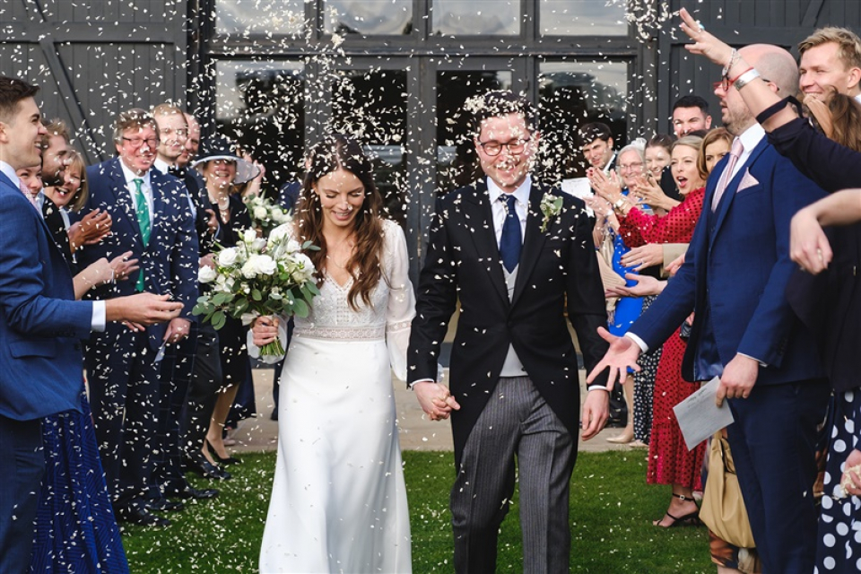 Une mariée et un marié du Suffolk partent de leur cérémonie de mariage au Royaume-Uni alors que des confettis leur sont lancés à l'extérieur de Bruisyard Hall Bruisyard Hall, couple de mariage Suffolk sortie de la cérémonie sous une pluie de confettis lancés par les invités
