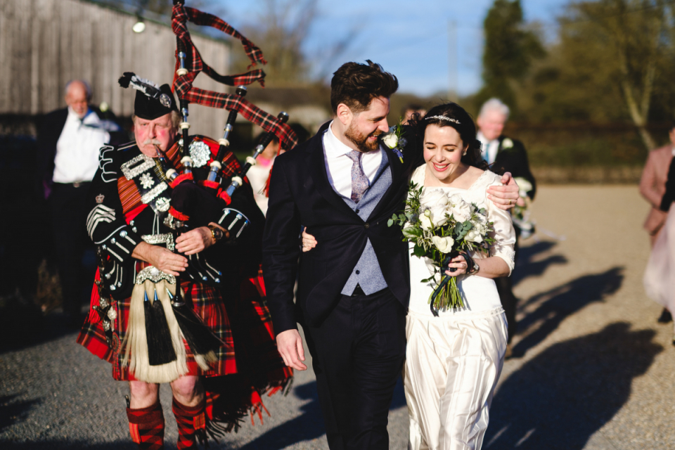 Le couple anglais se promène avec un joueur de cornemuse au lieu de mariage Bruisyard Hall dans le Suffolk, en Angleterre Les mariés du Suffolk marchent sur le terrain du Bruisyard Hall avec un joueur de cornemuse