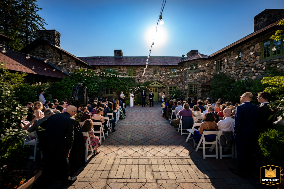 A picturesque wedding ceremony at Willowdale Estate in Topsfield, Massachusetts, in warm sunlight against a beautiful blue sky, with guests seated and watching the enchanting scene unfold.