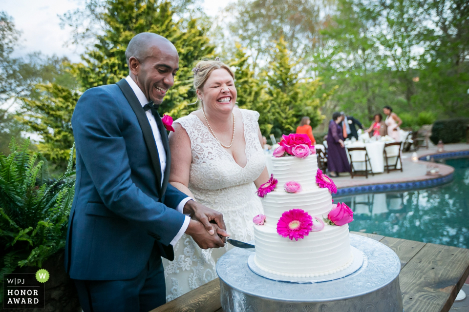 Foto von: <a href="https://www.wpja.com/contests/2018-v03-photography-competition/2182896"> Cindy Brown - Atlanta Georgia </a> Aska Farms, Blue Ridge, GA - Zeremonie zum Schneiden von Kuchen am Pool an dieser Rezeption im Freien