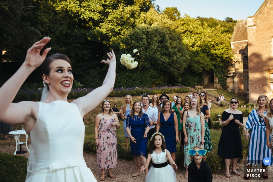 the Guests wait as the bride throws the bouquet outside Guests wait as the bride throws the bouquet outside at the wedding reception in St Audries Park