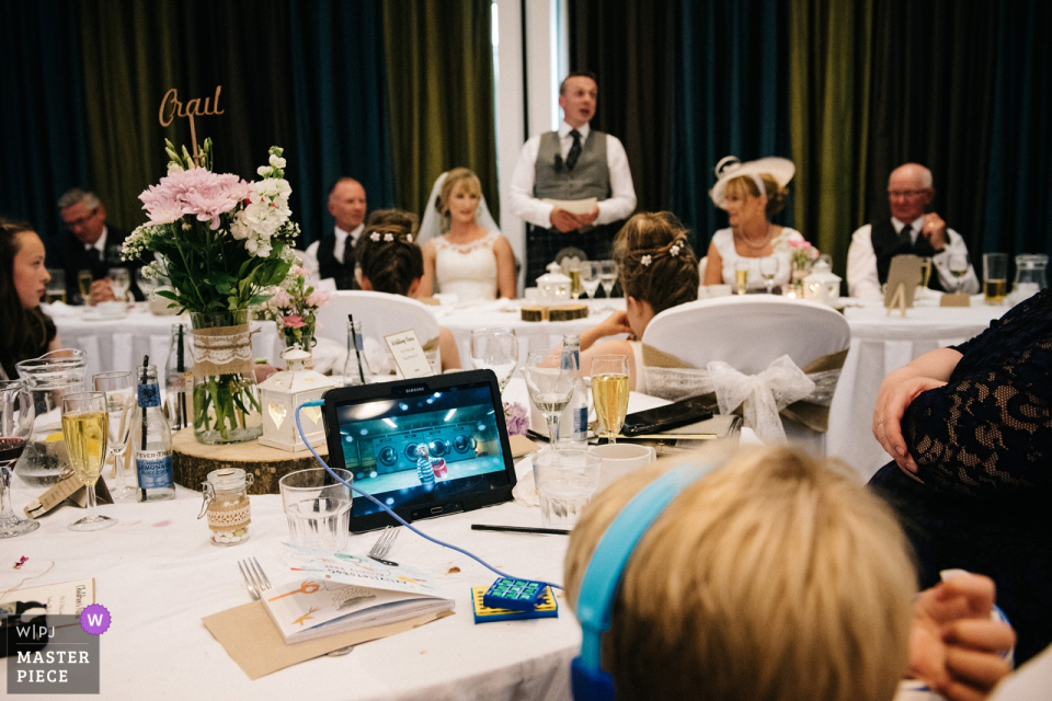a young wedding guest watches videos during the speeches