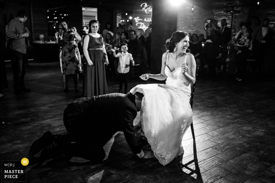 Foto: <a href="https://www.wpja.com/contests/2019-v02/best-wedding-photographers/2446426"> Milan Lazic - Chicago Illinois </a> Biagio evants Hochzeitsfotografie Strumpfband tanzen, um den Bräutigam zu beginnen, der das Strumpfband unter dem Kleid der sitzenden Braut fischt