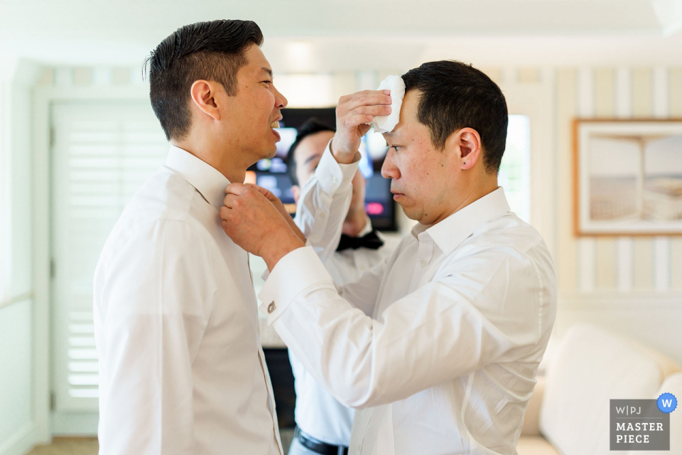 Photo by: <a href="https://www.wpja.com/contests/2019-v05/best-wedding-photographers/2483001">Alex Paul - Boston Massachusetts</a> Wequassett Resort Wedding Photographer | The Groom is helping his groomsmen to get ready with is tie and getting the sweat wiped from his brow by another