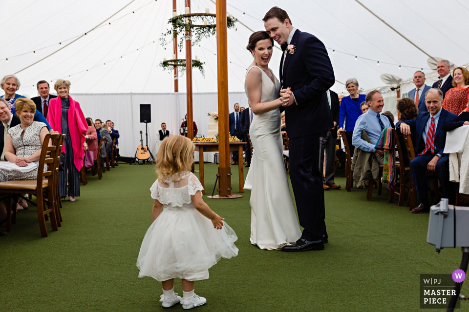 Photographie de mariage à la ferme en tentes de la mariée et le marié craquant à la fille de fleur qui a été attachée au côté de la mariée toute la journée Hardy Farm à Fryeburg dans le Maine Photographie de mariage | Les mariés craquent à la fille de fleur qui a été attachée aux côtés de la mariée toute la journée