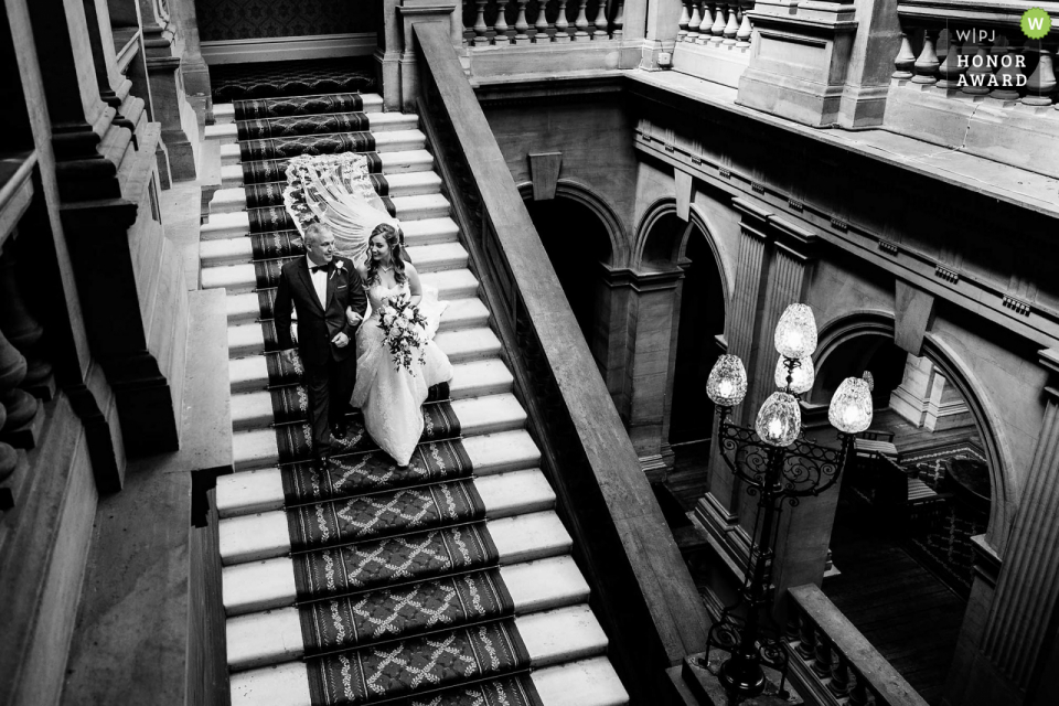 Heythrop Park, fotógrafo de reportaje de bodas en el Reino Unido: la novia y su padre bajando la gran escalera en Heythrop Park