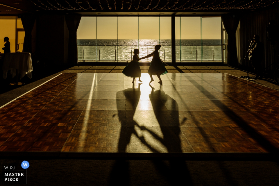 Zwei Blumenmädchen tanzen im Fenster Sandringham Yacht Club - Hochzeitsreportage-Fotografie Melbournes Australien - zwei Blumenmädchen, die in das Fenster tanzen