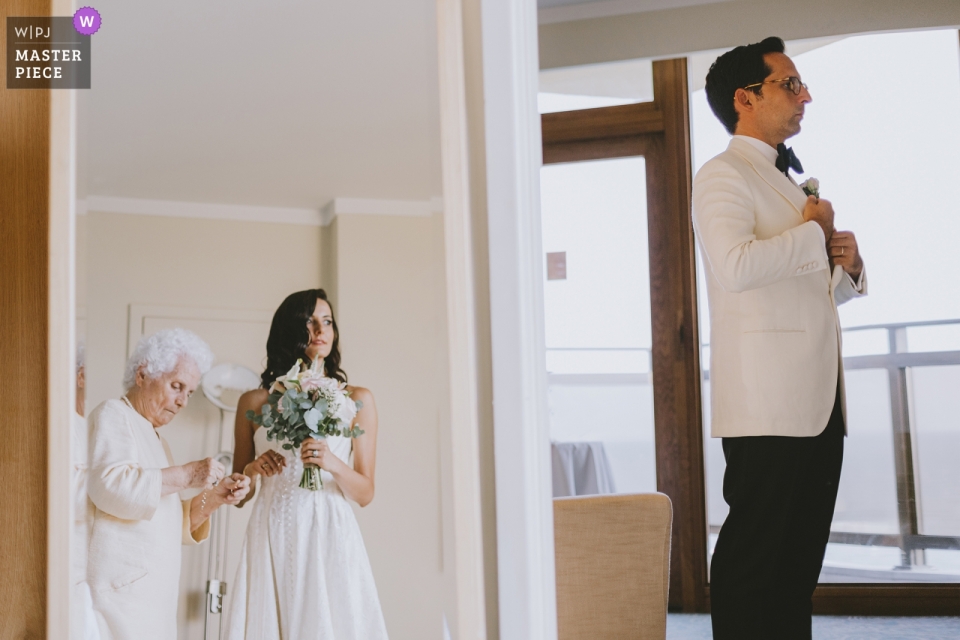 Photo: <a href="https://www.wpja.com/contests/2019-v09/best-wedding-photographers/2536726"> Emre Nesli - Istanbul Istanbul </a> Mersin, Hôtel Hilton / Mariage en Turquie Photos de la grand-mère de la mariée la préparant sur le miroir et du marié effectuant les dernières vérifications dans la pièce voisine