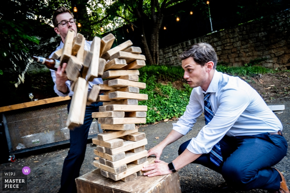 Foto: <a href="https://www.wpja.com/contests/2019-v10/best-wedding-photographers/2543704"> Joshua Grasso - Buford Georgia </a> Upstairs Atlanta Wedding Photos - Gäste spielen Jenga beim Hochzeitsempfang im Freien mit Spielen