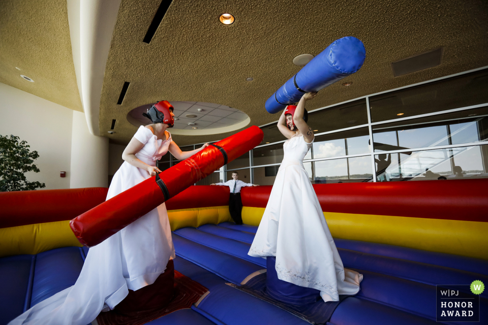 The brides partake in some pre-ceremony bounce house jousting at their wedding Monona Terrace, Madison, WI wedding venue photo | The brides partake in some pre-ceremony bounce house jousting at their wedding.