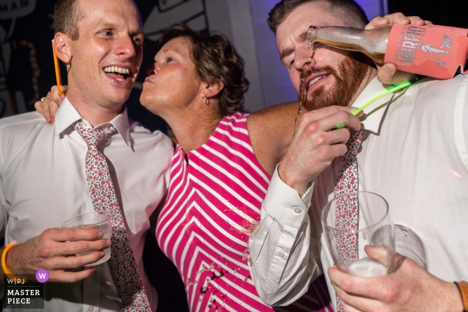 Foto: <a href="https://www.wpja.com/contests/2019-v11/best-wedding-photographers/2546395"> Joshua Grasso - Buford Georgia </a> Georgia - Monday Night Garage - Fotografie der Rezeption, in der Mama während einer Umarmung Bier auf ihre Kinder verschüttet.