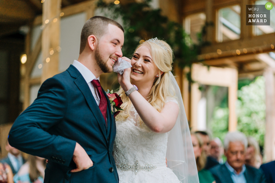 Sposo che piange e la sua lacrima asciugata dalla sposa Foto di Oak Tree Of Peeover durante la cerimonia al coperto | Lo sposo piange e si fa asciugare la lacrima dalla sposa