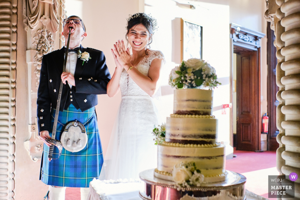 Foto: <a href="https://www.wpja.com/contests/2019-v14/best-wedding-photographers/2553388"> Ian Bursill - Loughborough Leicestershire </a> Der Bräutigam leckt die Buttercreme vom Schwert, nachdem er den Kuchen geschnitten hat. | Hochzeitsreportagefotografie von Beaumanor Hall, Loughborough, Großbritannien