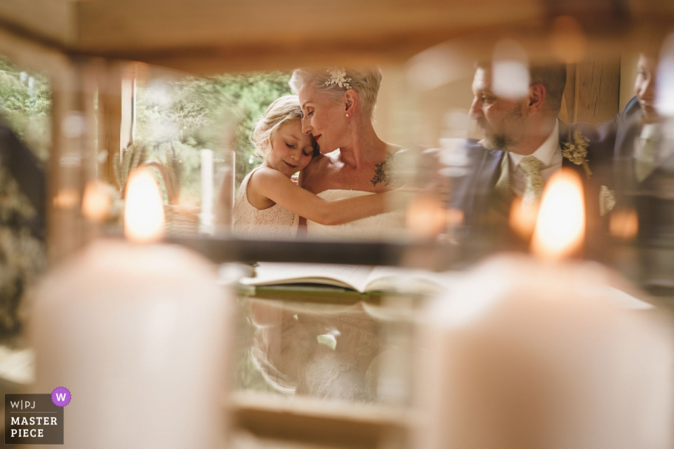 Photo by: <a href="https://www.wpja.com/contests/2019-v15/best-wedding-photographers/2555399">Phil Barrett - Ellesmere Shropshire</a> MILL BARNS Wedding Venue | Bride and daughter share a hug while Groom looks o