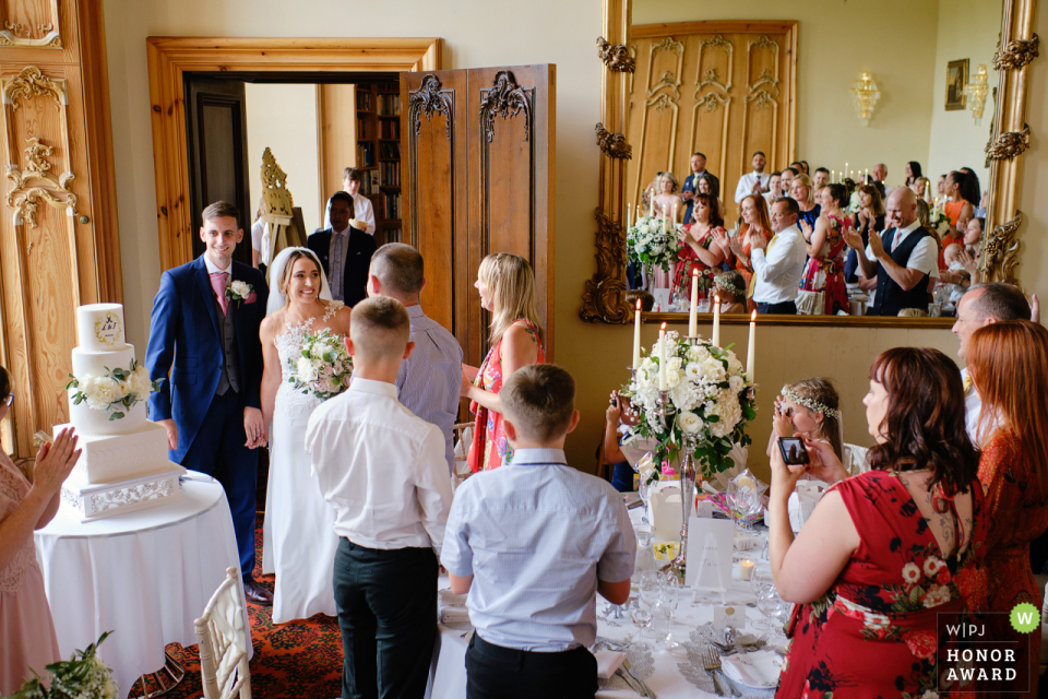 As the bride & groom entered the dining room Stoke Rochford Hall, Grantham, UK wedding venue photographer said this: As the bride & groom entered the dining room, I shot with the camera above my head to include the guests in the mirror.