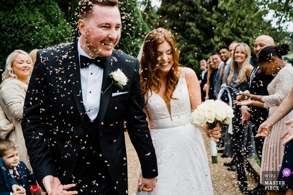 bride and groom walking down the aisle with a shower of confetti hitting them Brookfield Barn, West Sussex wedding ceremony of bride and groom walking down the aisle with a shower of confetti hitting them.