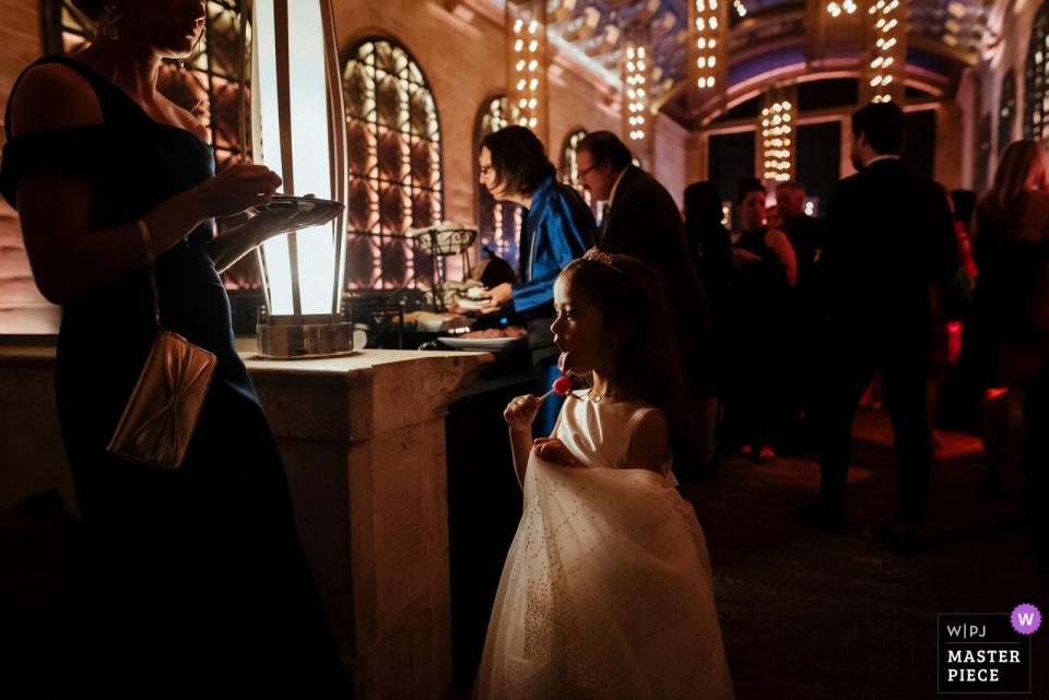 Foto door: <a href="https://www.wpja.com/contests/2019-v18/best-wedding-photographers/2568015"> Colleen Stepanian - Philadelphia Pennsylvania </a> Receptie Locatie Trouwfotografie: Union Trust, Philadelphia, Pennsylvania Bloemenmeisje slaagt erin om nog een lolly van haar moeder te krijgen tijdens het cocktailuurtje.