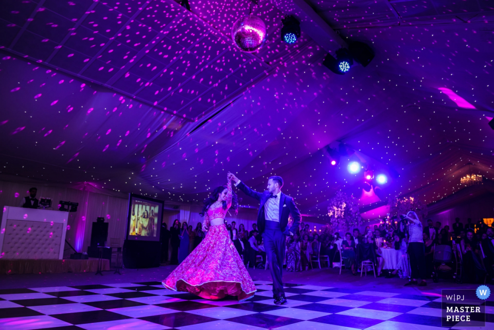 Fotografia de casamento na Inglaterra no local Ditton Park Manor | Primeira dança para a noiva e o noivo sob luzes roxas.