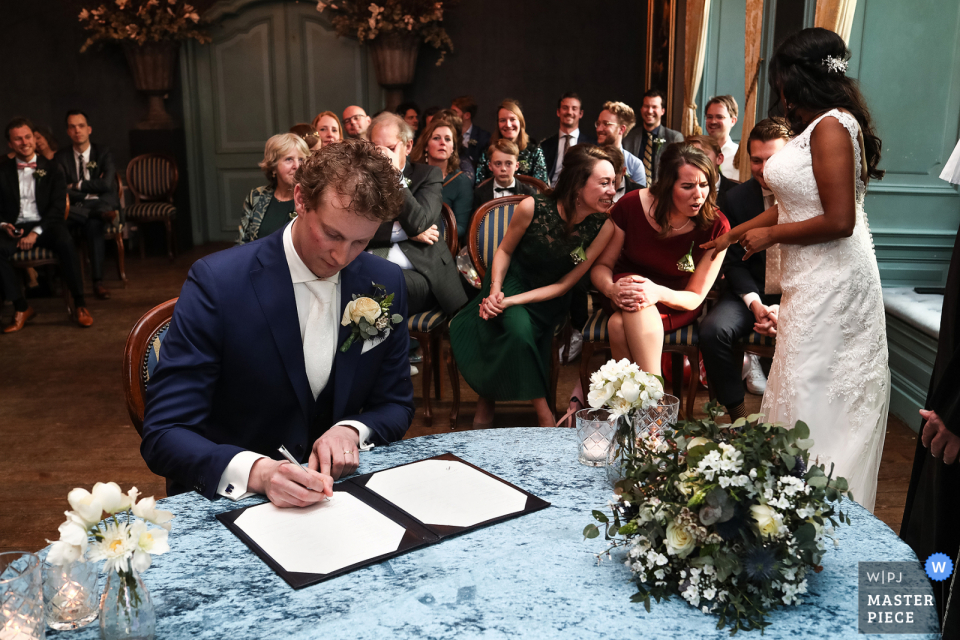 La mariée montre son alliance à ses meilleurs amis, tandis que son nouveau mari signe le certificat de mariage à Kasteel Wijenburg Echteld La mariée montre son alliance à ses meilleurs amis, tandis que son nouveau mari signe le certificat de mariage à Kasteel Wijenburg Echteld