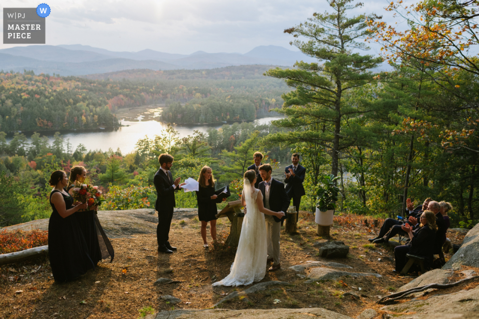 Forest Lake Camp in Chestertown, NY image of a couple embracing at the end of their ceremony on the side of a mountain as the sun gets low in the sky. Their wedding party and parents surround them. Forest Lake Camp in Chestertown, NY image of a couple embracing at the end of their ceremony on the side of a mountain as the sun gets low in the sky. Their wedding party and parents surround them.