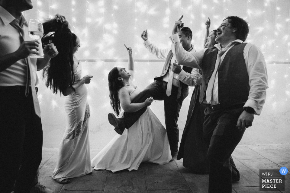 At Villa Orlando in Italy, during a lively rock 'n roll moment captured in black and white, the bride playfully strums an air guitar on a man's leg. This energetic and fun-filled scene encapsulates the spirited atmosphere of the dance party.