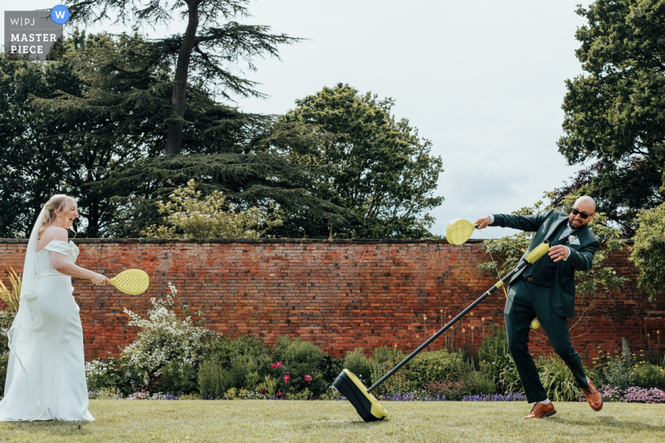   Laughter fills Thorpe Garden in Staffordshire, UK, as the bride delivers a playful swing ball hit to the groom, adding a spirited and lighthearted touch to the festivities.