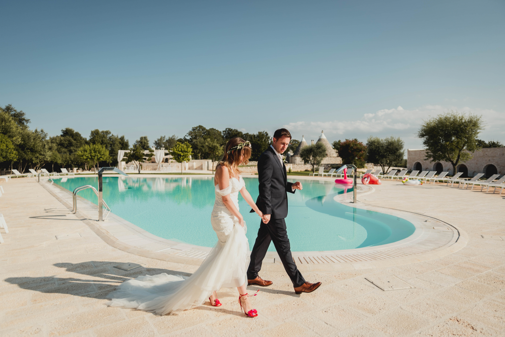 Image d'engagement de la région des Pouilles - se promener dans la piscine du complexe en tenant la main du marié Masseria Grieco Photographie de mariage - Région des Pouilles, Italie Photographie de fiançailles | La mariée brandit sa robe alors qu'elle se promène dans la piscine du complexe en tenant la main du marié