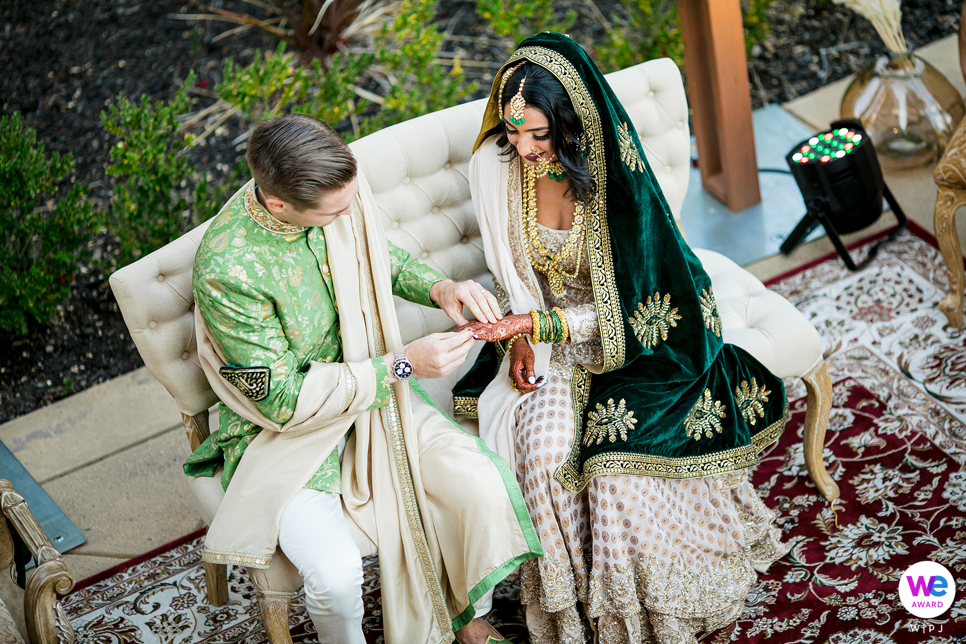 The bride and groom dressed in traditional clothing seated outdoors in a backyard, exchanging vows and rings in an intimate ceremony with close family and friends