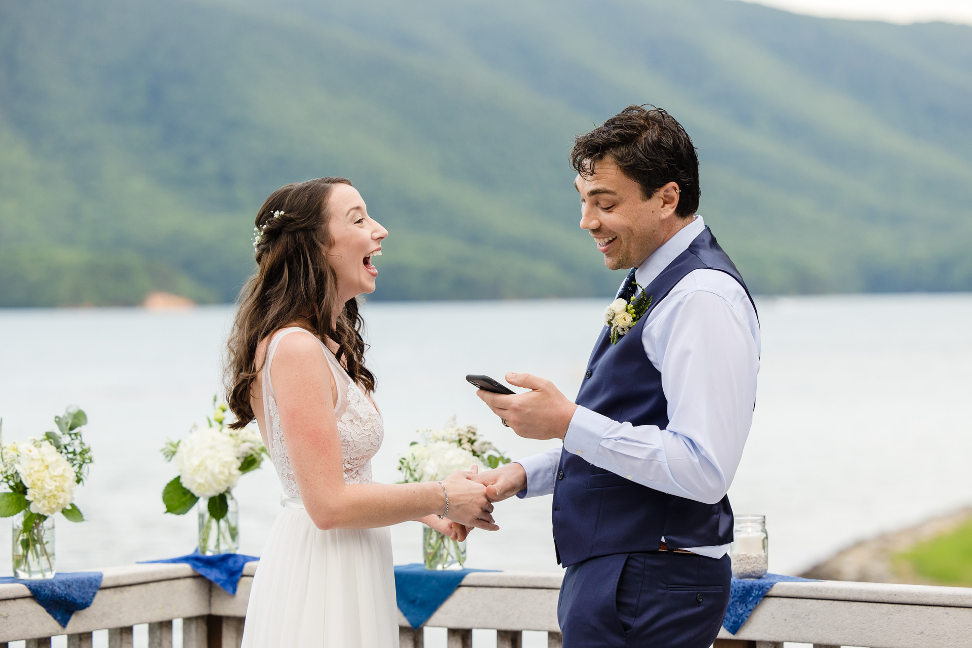 Bride and groom share joyful moment as groom reads vows from phone at Smith Mountain Lake.