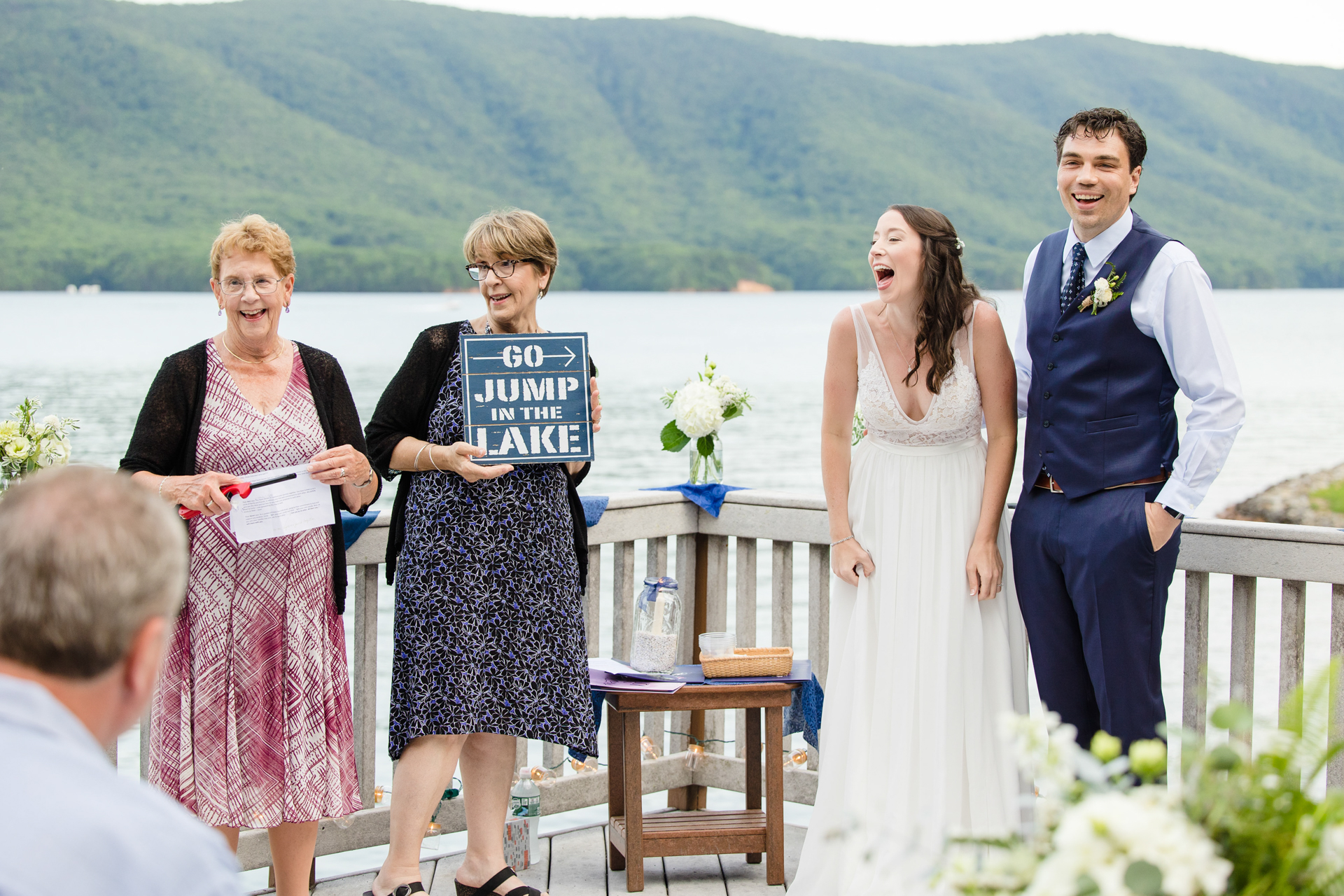 Officiant reveals cheeky "Go Jump in the Lake" sign, adding humor to the elopement ceremony.