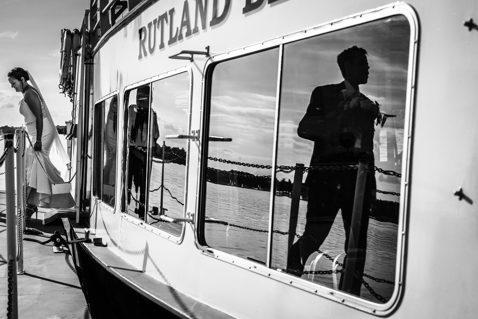 Newlyweds leave Rutland Belle ferry; groom's silhouette visible in the window, capturing farewell.
