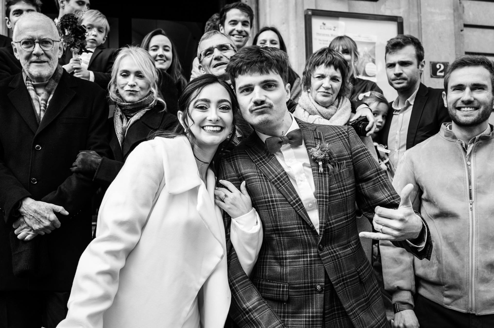 Smiling group crowds together for energetic photo; groom flashes carefree surfer hand sign in Lyon.